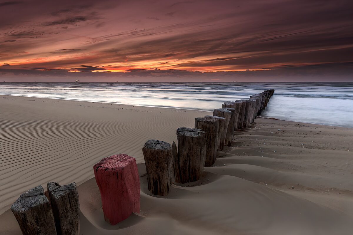 PDGIT8153069: Pali di legno sulla spiaggia al tramonto