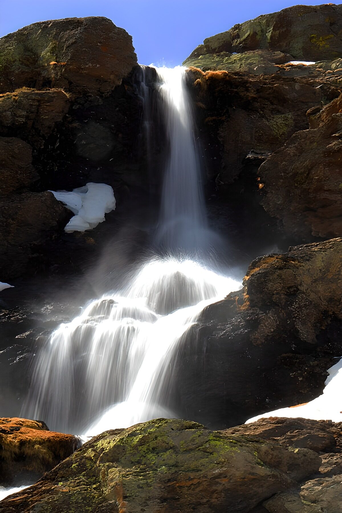 PDGIT2047076: Cascata al sole tra rocce scure e neve