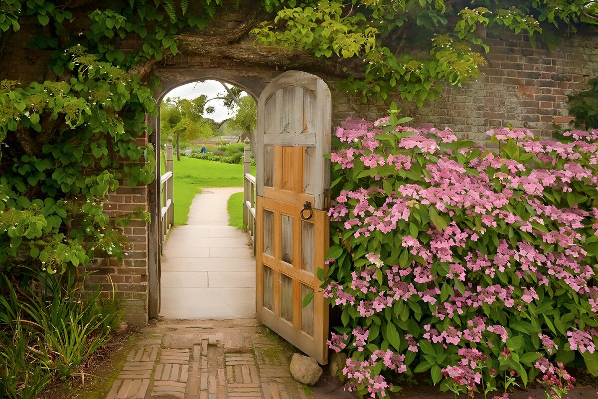 PDGIT8679661: Cancello aperto tra mattoni e fiori rosa