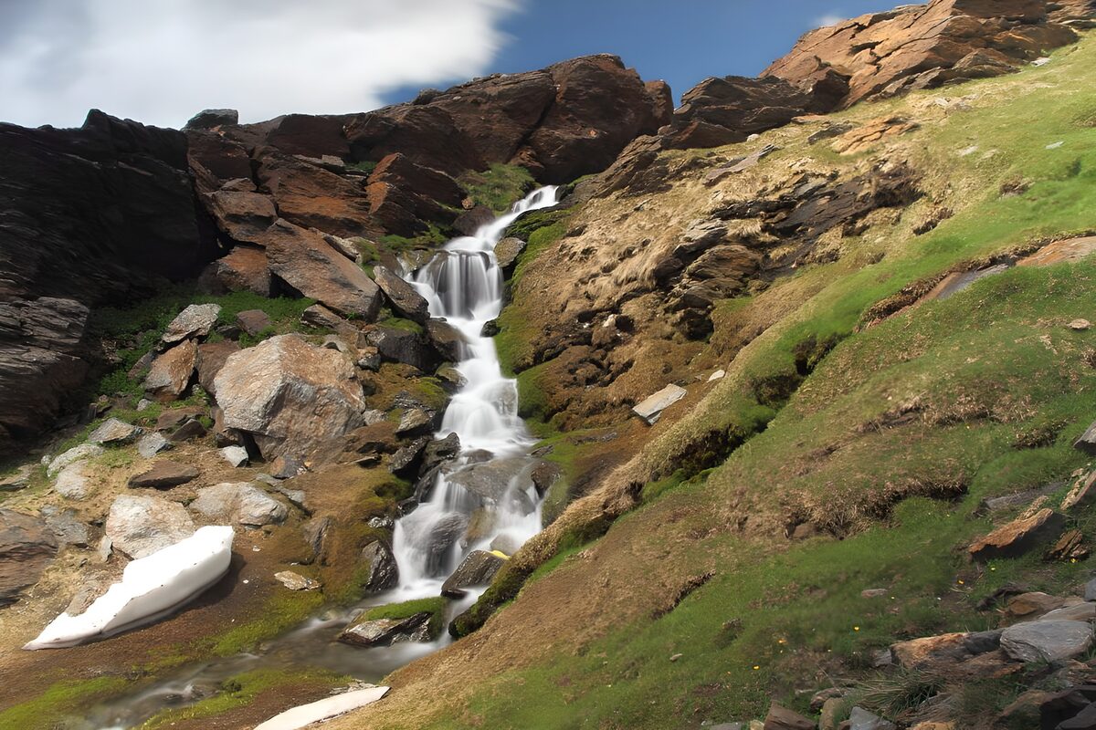 Cascata tra rocce e prati al sole