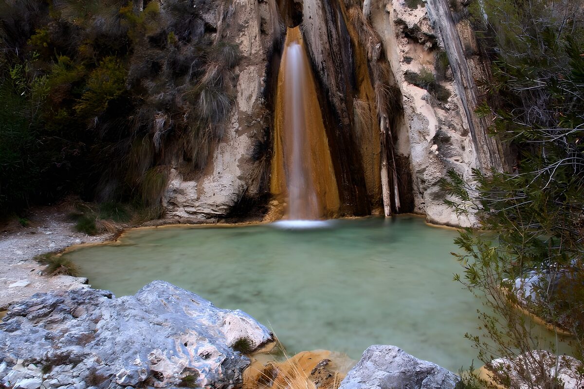 Cascata tra le rocce e pozza verde
