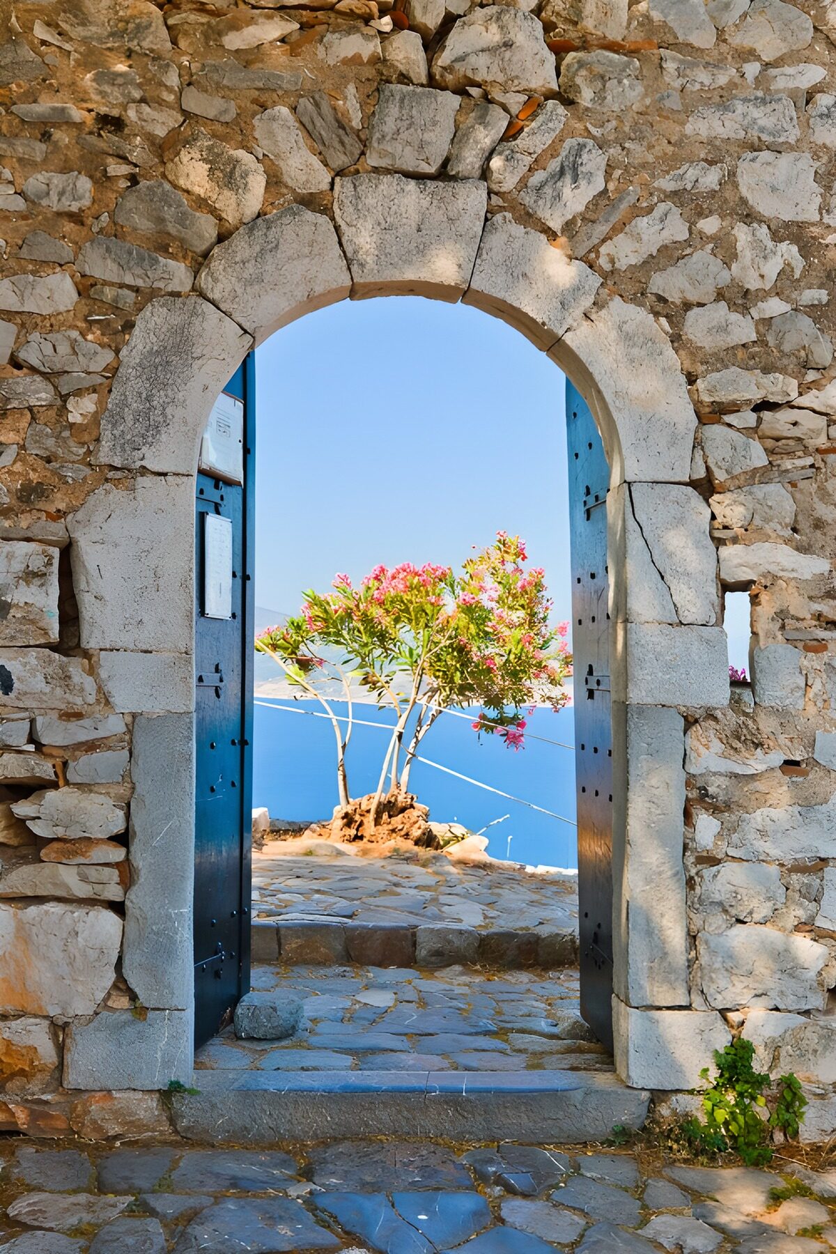 PDGIT7613626: Arco in pietra con porte blu sul mare